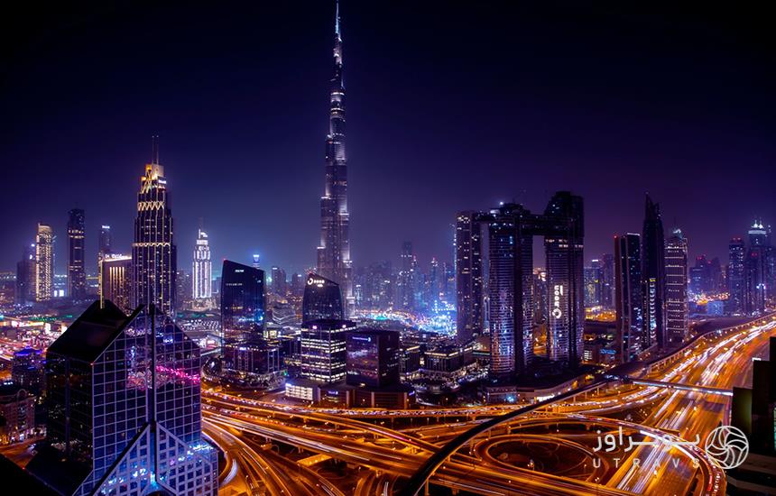خیابان‌های شهر دبی از بالا که در شب با نورهای شهری روشن شده‌اند.